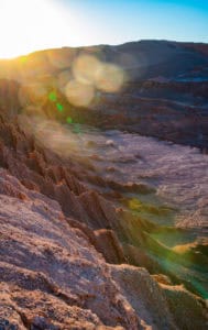 Sunset illuminating rugged volcanic terrain with warm light and lens flare.