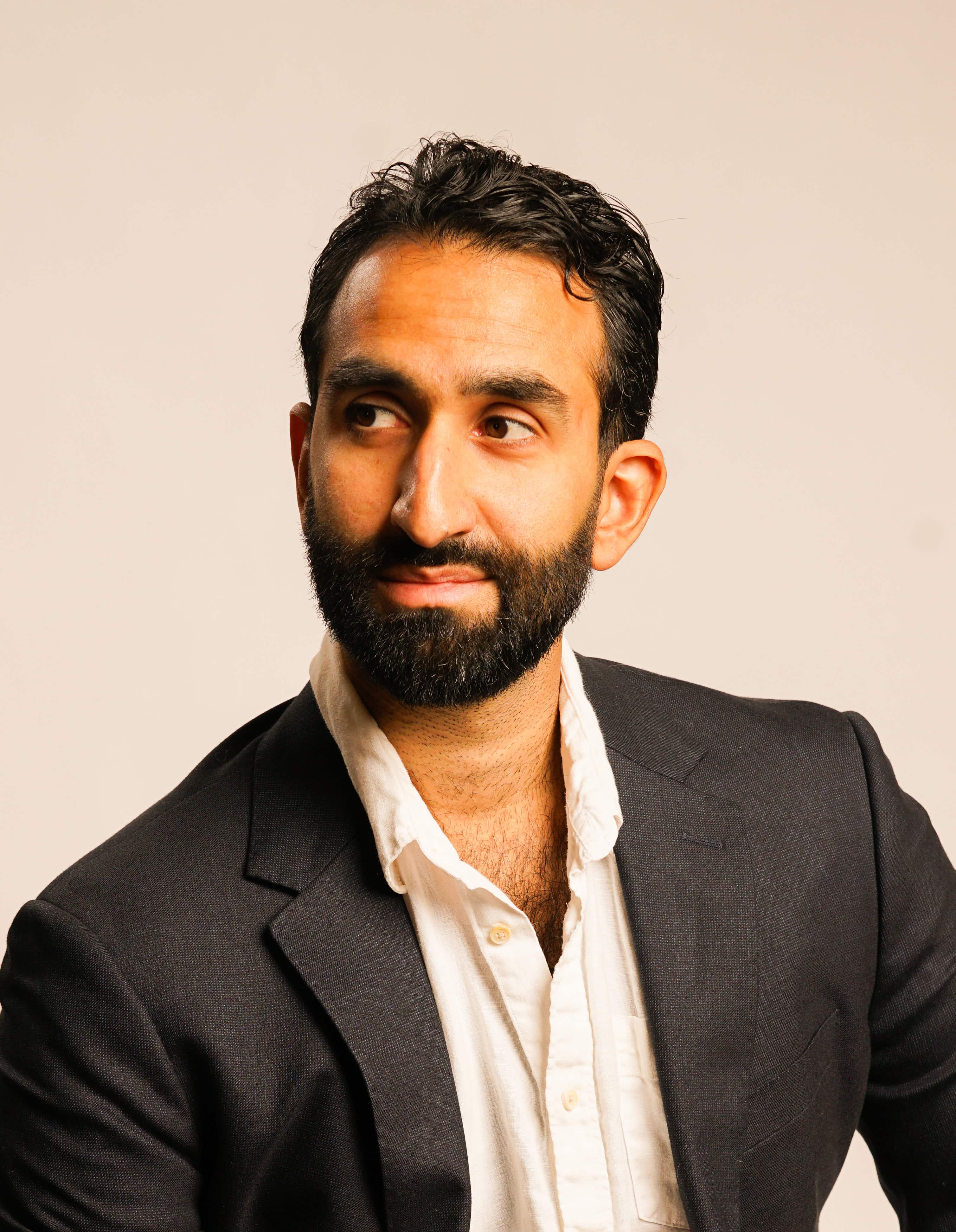 Manick Bhan, a confident professional in a dark suit, looking thoughtfully to the side.