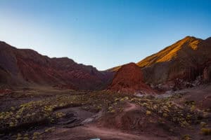 Volcanic landscape with colorful hills and sparse vegetation under a clear sky.