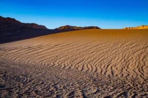 Sand dunes and mountain backdrop in a vast desert scene.