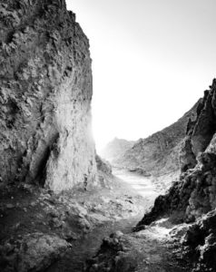 Black and white photo of a rugged mountain canyon with steep rocky walls.