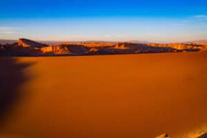 Breathtaking desert landscape with orange dunes and distant mountains at sunset.