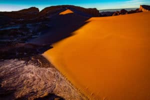 Desert dunes with golden sand under a vibrant sunset sky.