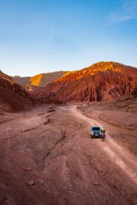Scenic view of vibrant desert mountains at sunset with a vehicle and cyclist in the foreground.