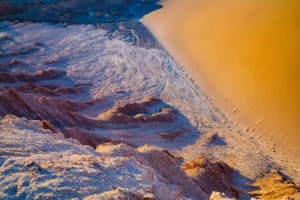 Beach shoreline with sand and waves at sunset.