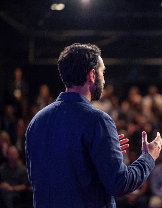 Manick Bhan delivering a speech at a conference with an engaged audience.